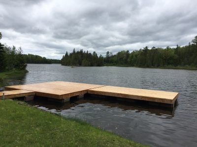 A wooden dock extends over a calm lake surrounded by trees under a cloudy sky.