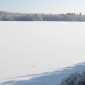 A frozen lake covered in snow with trees along the shoreline under a clear, pale blue sky.